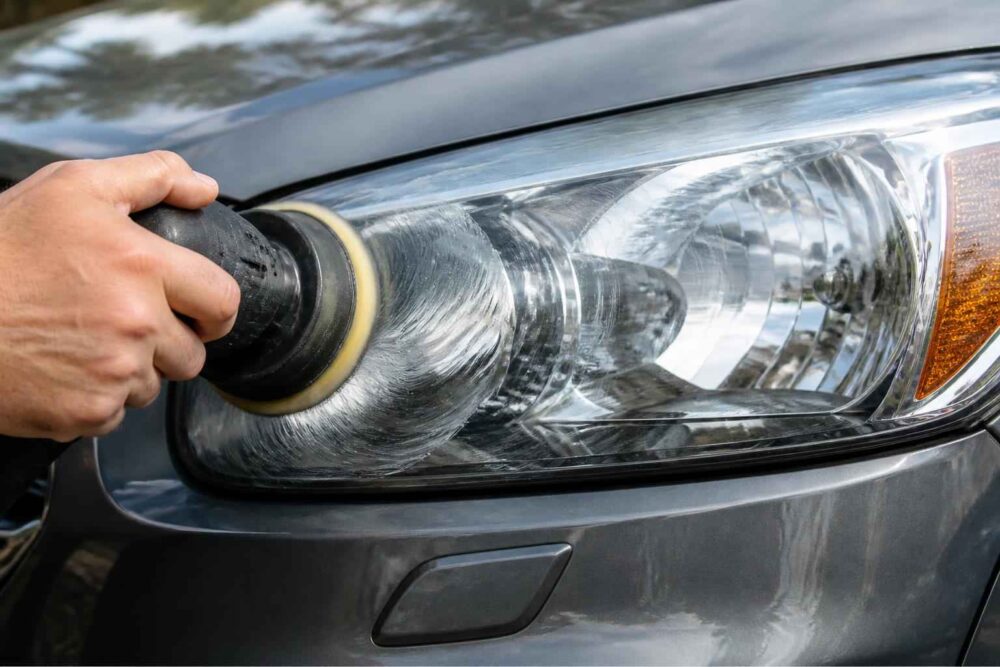 Dłoń polerująca reflektor przedni samochodu za pomocą elektrycznej polerki