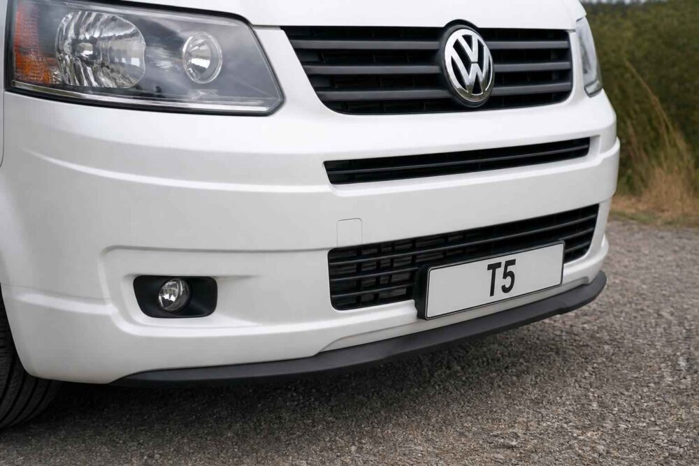 Przedni fragment białego Volkswagena T5 z grillem, reflektorem i tablicą rejestracyjną T5