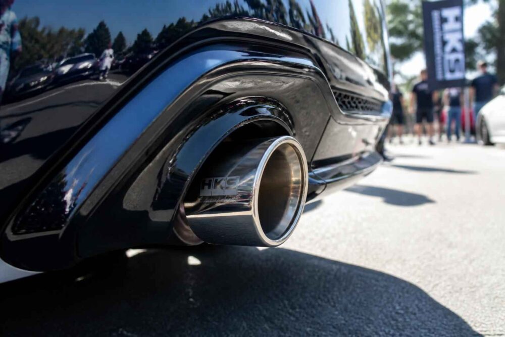 Zbliżenie na chromowaną końcówkę wydechu czarnego samochodu sportowego podczas plenerowego wydarzenia motoryzacyjnego